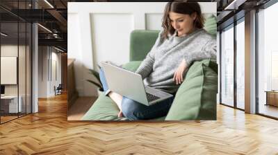 Young beautiful smiling woman using laptop lying on the couch. Concept of freelance job, home office. Female using technology for learning, shopping, e-commerce, communication, social media Wall mural