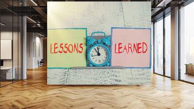 Handwriting text Lessons Learned. Conceptual photo the knowledge or understanding gained by experience Mini blue alarm clock standing above buffer wire between two notation paper Wall mural