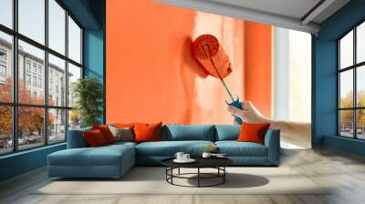 Male hand painting wall with paint roller. Painting apartment, renovating with red orange color paint Wall mural