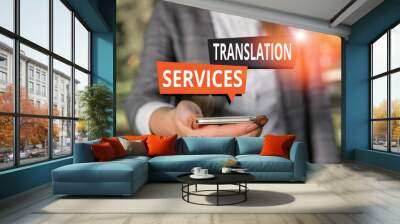 Text sign showing Translation Services. Business photo showcasing organization that provide showing to translate speech Woman in grey suites holds mobile phone Wall mural