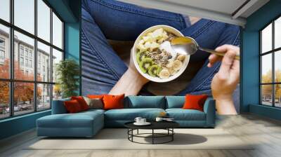 Eating healthy breakfast bowl. Yogurt, buckwheat, seeds, fresh fruits in white bowl in woman' s hands. Clean eating, dieting, detox, vegetarian food concept Wall mural