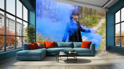 Young woman in forest having fun with blue smoke grenade, bomb Wall mural