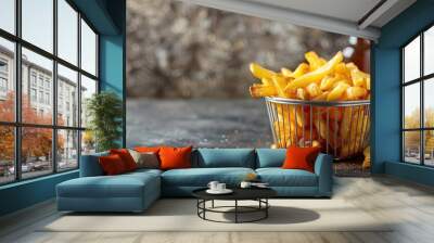 Crispy golden French fries in metallic basket with blurred background, seasoning visible Wall mural