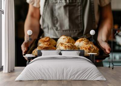 Person in apron holding a baking tray with golden pastries kitchen setting Wall mural