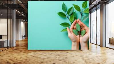 Two hands holding green leaves against turquoise background Wall mural