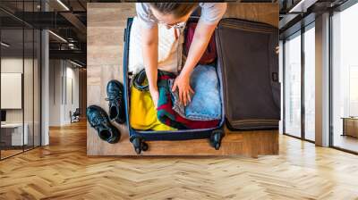 Woman packing her clothes into a suitcase at home in the living room. View from above. Travel concept. Vacation preparation. The process of packing a suitcase on vacation or on a business trip. Wall mural