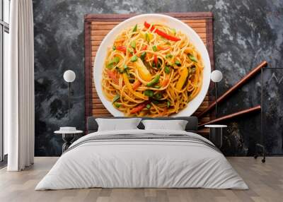 Schezwan Noodles or vegetable Hakka Noodles or chow mein is a popular Indo-Chinese recipes, served in a bowl or plate with wooden chopsticks. selective focus Wall mural