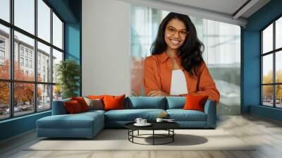 Portrait of  smiling African American business woman wearing stylish eyeglasses looking at camera standing in modern office. Successful business and career concept  Wall mural