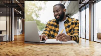 Young handsome African American man using laptop computer, taking notes, planning start up, working online. Portrait of happy student studying, learning languages, online education concept Wall mural