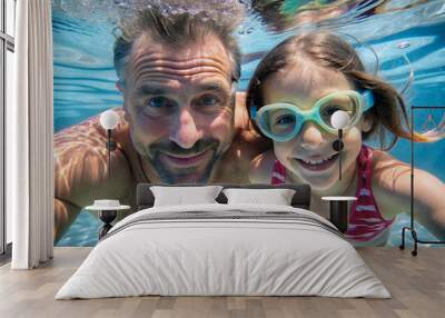 A daughter and father in goggles swims underwater in the clear water and looking at camera. Happy vacation with family. Wall mural