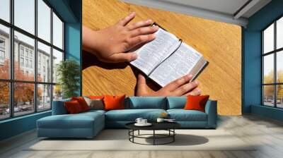 Childs hands hold a bible leaning on a wooden table. Book Holy Bible.Kid reading from the holy bible,close up. Wall mural