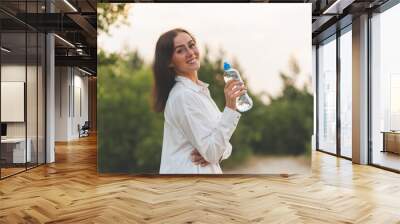 Girl drinks water from a plastic bottle.young caucasian woman in nature forest in woods while holding bottle of water Wall mural