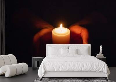 Hands holding burning candle in dark like a heart.Selective focus,black background. Wall mural