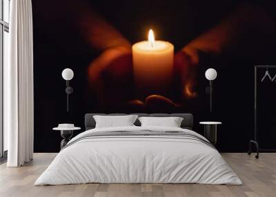 Hands holding burning candle in dark like a heart.Selective focus,black background. Wall mural