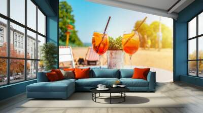 Two glasses of orange spritz aperol drink cocktail on table outdoors sunset with sea and trees view blurred background. Wall mural