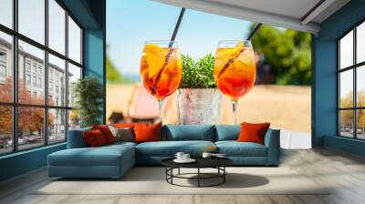 Two glasses of orange spritz aperol drink cocktail on table outdoors with sea and trees view blurred background. Wall mural