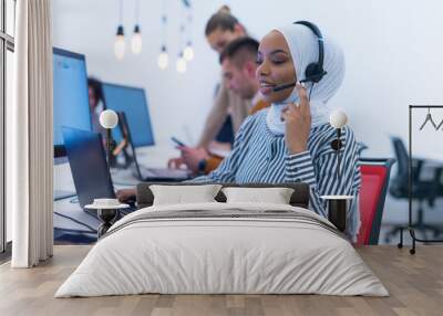 African muslim female with hijab scarf customer representative business woman with phone headset helping and supporting online with customer in modern bright call centre. Wall mural