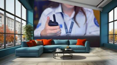 Security guard monitoring modern CCTV cameras in surveillance room. Female security guard in surveillance room. Female security guard holding portable radio in hand at workplace. Wall mural