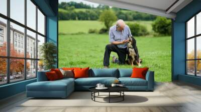 My closest friend. Shot of a cheerful mature farmer kneeling and holding his pet dog outside on a green field. Wall mural