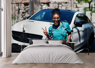 African american doctor female at lab coat with stethoscope posed outdoor against white suv car. Wall mural