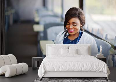 african american doctor female with stethoscope looked at phone and sitting on clinic. Wall mural