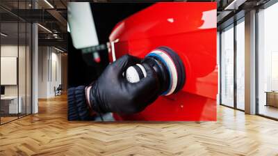 Car detailing concept. Hands of man with orbital polisher in repair shop polishing orange suv car. Wall mural