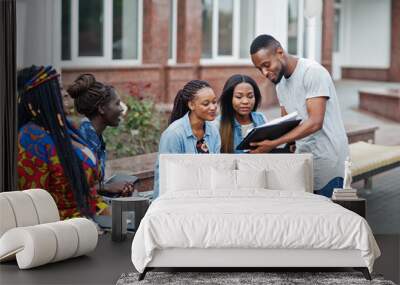 Group of five african college students spending time together on campus at university yard. Black afro friends studying at bench with school items, laptops notebooks. Wall mural