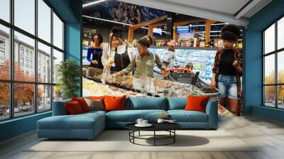 Group of five african womans with shopping carts choose cheese in supermarket. Wall mural