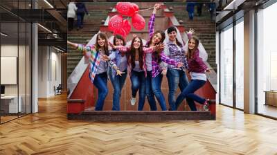 Group of six girls having fun at hen party, with balloons under rain at stairs of city. Wall mural