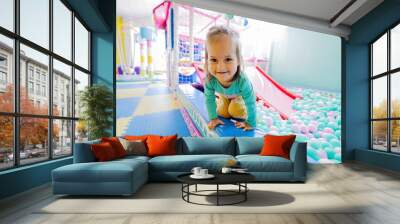 Happy girl playing at indoor play center playground. Color balls in ball pool. Wall mural