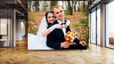 Happy wedding couple sitting at autumn forest with fell leaves f Wall mural