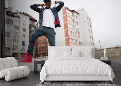 Portrait of jumping stylish african american man on sportswear, cap and glasses. Black men emotion model street fashion. Wall mural