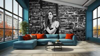 Red haired punk girl wear on black dress at the roof against brick wall with iron ladder. Wall mural