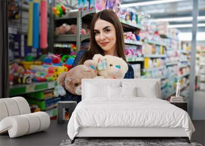 Shopping woman looking at the shelves in the supermarket.  Portrait of a young girl in a market store holding small soft toys. Wall mural