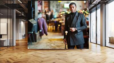 Stylish african american gentleman in elegant black jacket, holding retro walking stick as cane flask or tippling cane with golden diamond ball handle. Rich fashionable afro man. Wall mural