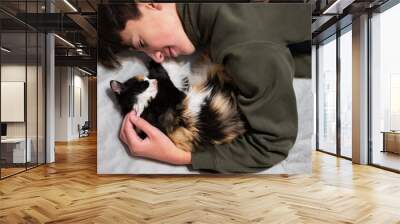 Teenager boy with kitty lying on the sofa. Children's love for pets. Wall mural