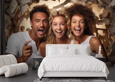 Three joyful friends seemingly burst through a beige wall, expressing excitement and fun Wall mural