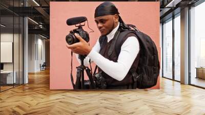 Young professional african american videographer holding professional camera with pro equipment. Afro cameraman wearing black duraq making a videos. Wall mural