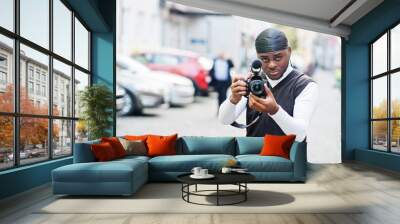 Young professional african american videographer holding professional camera with pro equipment. Afro cameraman wearing black duraq making a videos. Wall mural