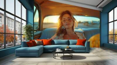 Young stylish woman lounges comfortably in the backseat of a vintage car, bathed in the warm glow of a sunset. Her relaxed pose and fashionable attire highlight a moment of serene escapism. Wall mural