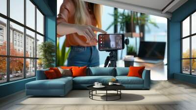 A woman's hand is pointing at the phone on top of an tripod Wall mural