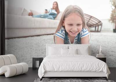 cute little girl with smartphone lying on the carpet in the living room Wall mural