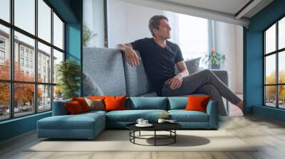 friendly young man sitting on the couch in his living room Wall mural