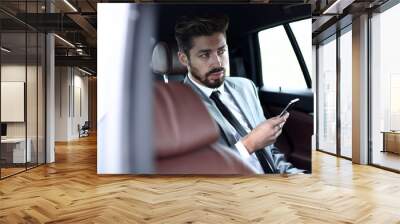 man in suit sitting in car and reading messages on smartphone Wall mural