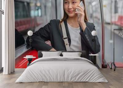 Asian businesswoman talking on phone while on the way traveling to the airport in a metro skytrain Wall mural