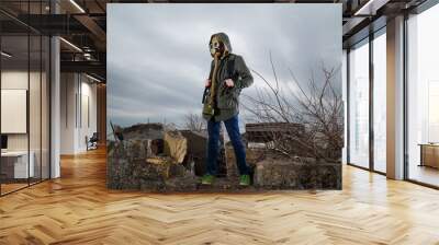 Human in gas mask standing among ruins and dramatic sky background. Enviromental pollution, ecology disaster, radiation, biological hazard concept. Wall mural