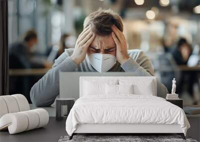 stressed young man in medical mask working with laptop at workplace in office Wall mural