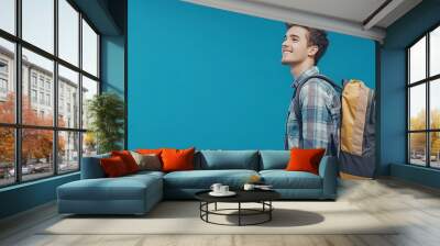 Young man with backpack over blue wall smiling and looking to the side Wall mural