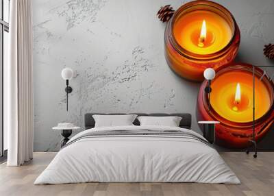 Two burning candles in glass jars on a white textured surface. Wall mural