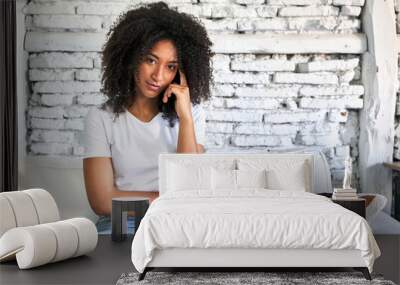 A young african american woman sitting on her sofa pointing temple with finger, thinking, focused on a task. Wall mural